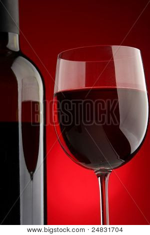 แก้วไวน์เต็มและขวด closeup แยกต่างหากบนพื้นหลังสีแดง