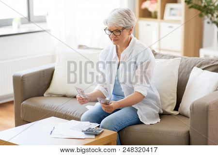 finances, savings, annuity insurance and people concept - senior woman with calculator and bills counting money at home