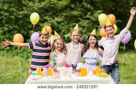 holidays, childhood and celebration concept - happy kids hugging on birthday party at summer garden