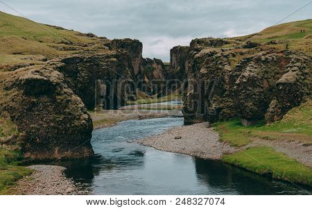 Fjadrargljufur Canyon In Iceland With Blue Water And Cloudy Sky