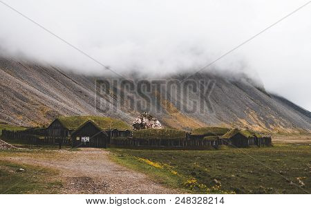 Old Viking Village In Iceland With Foggy Hill. Old Wooden Buildings Covered Grass