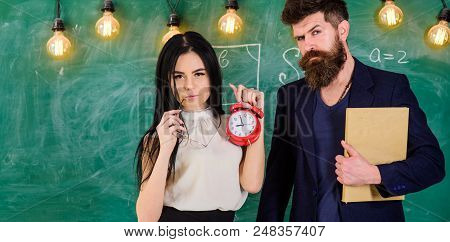 Man With Beard Hold Book And Sexy Girl Teacher Holds Alarm Clock, Chalkboard On Background. School R