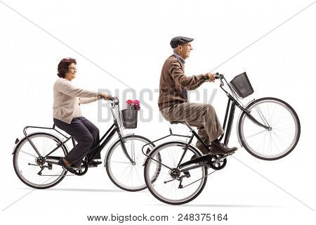 Elderly woman and an elderly man riding bicycles with the elderly man doing a wheelie isolated on white background