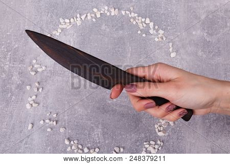 A Hand With A Wooden Knife Is Situated On The Grey Tabletop, Surrounded With White Decorations.