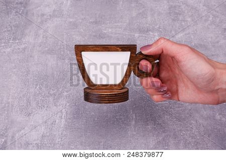 A Hand Is Holding A Wooden False Cup With White Centre On The Grey Background.