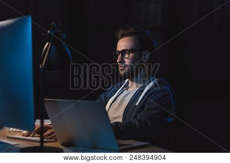 Young Programmer In Eyeglasses Working With Desktop Computer And Laptop At Night