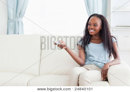 Mulher sorridente no sofá mudando de programa de TV