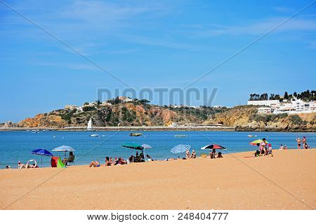 Albufeira, Portugal - June 10, 2017 - Tourists Relaxing On The Beach With Town Buildings To The Rear