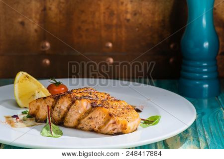 Close-up Tasty Cooked Salmon On A White Plate With Lemon, Tomato And Bay Leaves, On A Wooden Table. 