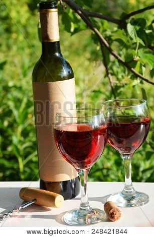 Red Wine Poured Into Wine Glass On Background Of Green Tree Leaf Foliage. Purpie Flower