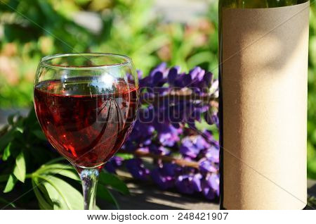 Red Wine Poured Into Wine Glass On Background Of Green Tree Leaf Foliage. Purpie Flower