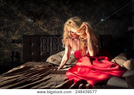 Beautiful Girl Sits On The Bed In Early Morning. Young Sleepy Woman Relaxes In Stylish Bedroom In Su