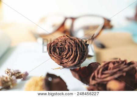 Selective Focus Withered Old Rusty Brown Roses And Love Word  On Blank White Book With Blurry Glasse