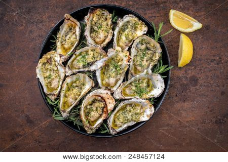 Barbecue overbaked fresh opened oyster with garlic, lemon and herbs offered as top view on a tray 