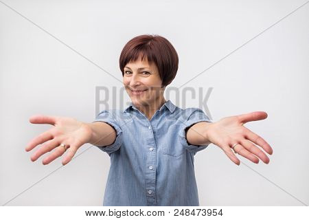 Portrait Of Attractive Mature Woman Raised Up Arms Hands At You. She Is Dressed In Blue Shirt. Happy