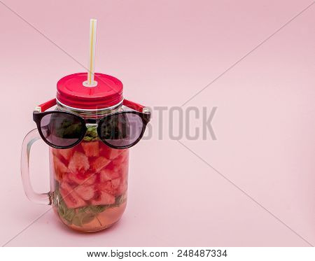 Glasses Lying On A Jar Of Cold Fresh Lemonade With Piece Of Watermelon And Ice On Pink Background.