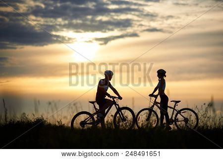 Two Cyclists, Guy And Girl Standing Opposite Each Other And Posing With Bikes. Silhouettes Of Couple