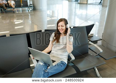 Young Smiling Traveler Tourist Woman With Headphones Listening Music Working On Laptop, Wait In Lobb