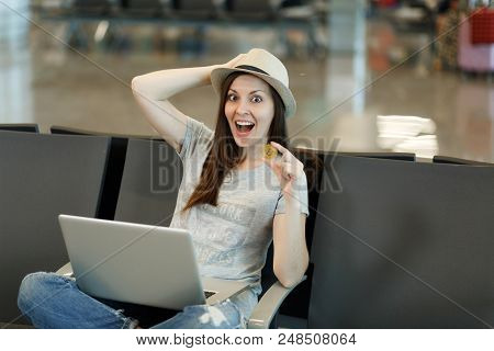 Young Surprised Traveler Tourist Woman In Hat Sitting, Working On Laptop Holding Bitcoin, Clinging T