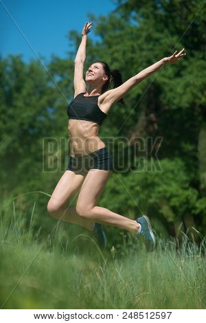 Young Woman Jumping On Background Of Trees. The Girl Is Engaged In Sports.