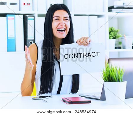 Young Angry Female Office Worker Ripping Contract At The Desk.
