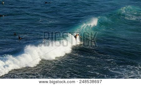 A Man Surfing On White Foam Wave In Blue Ocean With People Swimming In Background At Tamarama Beach,