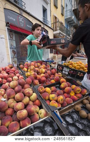 Briancon, France, 10 June 2018: Boy Sells Fruit On Open Air Market Of Briancon In The French Haute P