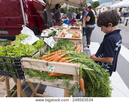Briancon, France, 10 June 2018: Boy Checks Vegetables On Open Air Market Of Briancon In The French H