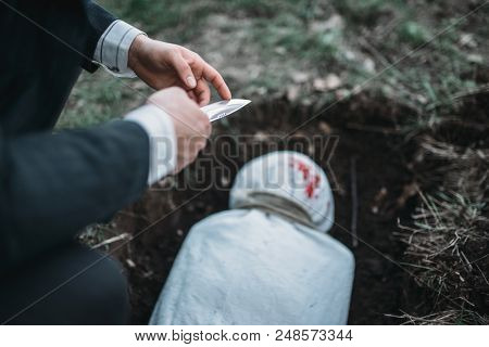 Slayer against grave, victim wrapped in a canvas