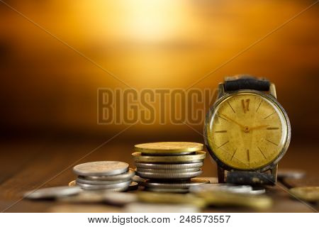 Time Is Money. Coins On Each Other And An Old Wristwatch. With Light Background, Illuminated In The 