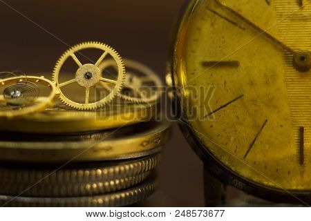 Time Is Money. Close-up Of Stacked Coins, An Old Wristwatch And Some Small Metal Gears With Dark Bac
