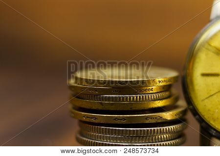 Time Is Money. Close-up Of Stacked Coins And An Old Clock. There Are More Empty Spaces In The Pictur