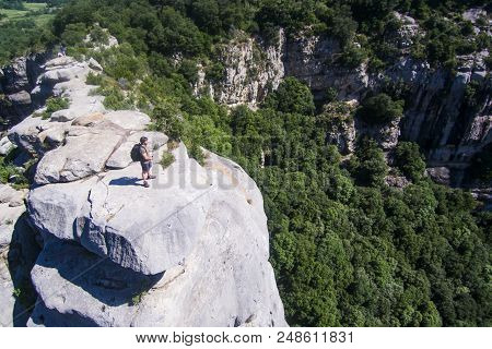Risky Mountaineer On A Cliff Looking At The Horizon. Aerial View