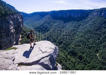 Risky Mountaineer On A Cliff Looking At The Horizon. Aerial View