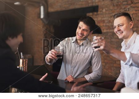 Handsome Smiling Friends Drinking Whiskey And Communicating With Cheerful Bartender In Pub, Copy Spa