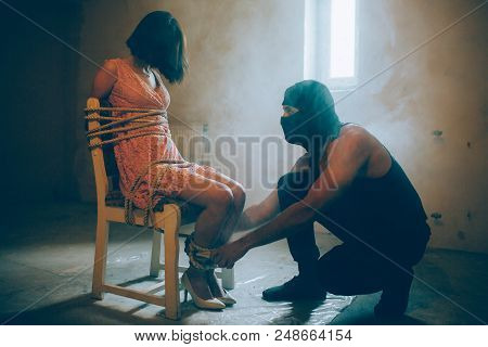 A Picture Of Kidnapped Girl Sitting On Chair. She Is Tied With Ropes. Her Hands And Legs Are Tied. H