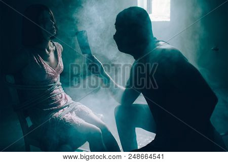 Tired And Serious Brunette Is Looking At Her Kidnapper. She Is Tied To Chair With Ropes. Killer Is L