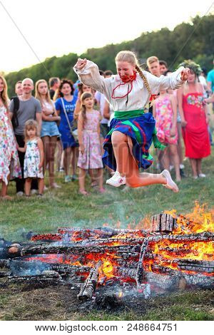 Kyiv, Ukraine - July 6, 2018: Young Girl In National Clothing Jumps Over The Flames Of Bonfire Durin