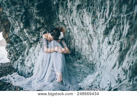 A Woman In A Long Dress Sitting Near The Sea