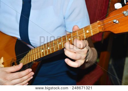 The Boy Plays The Guitar And Takes Chords, Dombra On The Background Of The Piano.