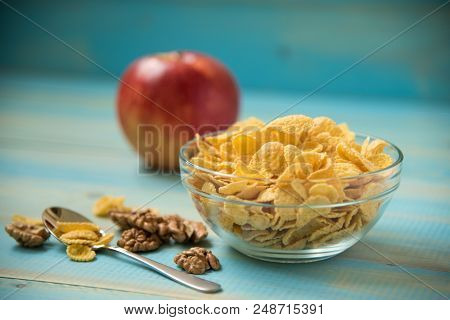 Tasty Cornflakes Wit Walnut And Apple In Glass Bowl On Blue Background. Corn Flakes. Healthy Breakfa
