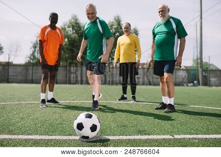 Selective Focus Of Football Ball And Multicultural Elderly Men On Green Football Field