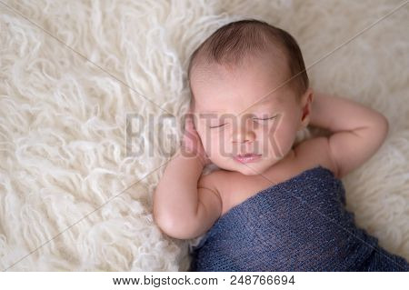 Headshot Of A Sleeping, Two Week Old Newborn Baby Boy Swaddled In A Navy Blue Wrap. Shot In The Stud
