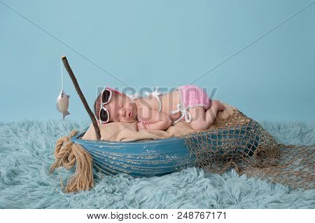 Portrait Of A Nine Day Old Newborn Baby Girl. She Is Sleeping In A Miniature Fishing Boat And Wearin