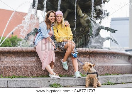 Young Happy Woman Embracing Female Friend With Yorkshire Terrier In Front Of Neptunbrunne, Berlin, G