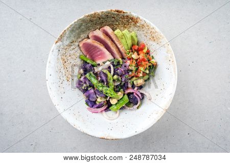 Modern fried tuna fish sashimi filet salad with green asparagus blue potatoes und vegetable chili relish as top view on a plate with copy space 