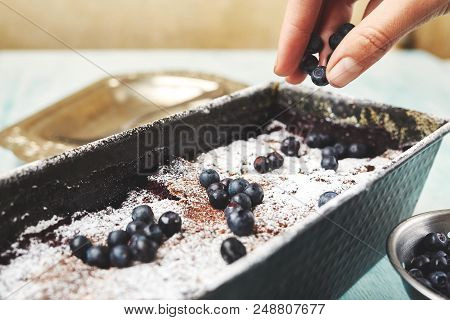 Berry Crumble In The Baking-tin And Small Bowl With Blueberries On The Blue Wooden Table. Woman Spri