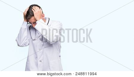 Handsome young doctor man suffering from headache desperate and stressed because pain and migraine. Hands on head.