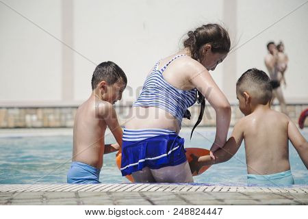 A Girl And Little Boy Sitting By The Pool. Summer Vacation Concept. Space For Text.