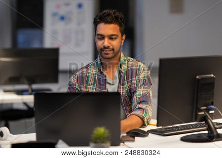 deadline, technology and people concept - creative man with laptop computer working at night office